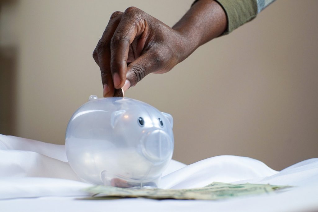 A person putting money in to a silver piggy bank